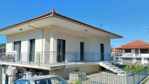 Un immeuble de deux étages doté d’un balcon, d’un escalier et d’une voiture garée devant.