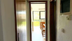 Un couloir menant à une cuisine avec une fenêtre, une porte et un interrupteur sur le mur.