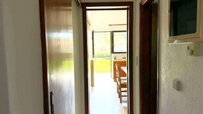 Corredor que dá para uma cozinha, com uma janela, uma porta e um interruptor de luz na parede.