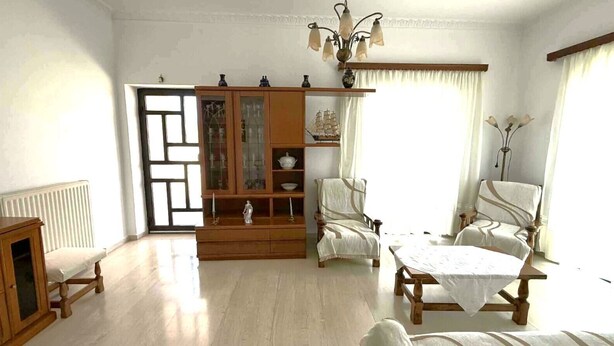 Une pièce comprenant un meuble en bois, deux fauteuils rembourrés, une table et un radiateur.