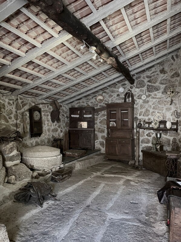 A rustic room with a stone wall, wooden beams, a wooden bench, a wooden cabinet, and a clock.