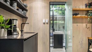 A modern kitchen with a coffee machine, shelves with dishes, and a view through a glass door. - Mirror House Escape + Sauna/Cold Plunge (Macon)