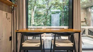 A dining area with a wooden table and black chairs, large windows with a view of a forest. - Mirror House Escape + Sauna/Cold Plunge (Macon)