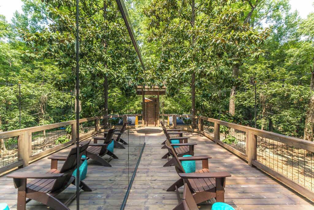 Eine Holzterrasse mit Sitzgelegenheiten und einer zentralen Struktur, umgeben von dichtem Baumbestand.