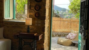 Quarto rústico com uma máquina de costura, janela com cortinas de renda, abajur e vista para uma encosta.