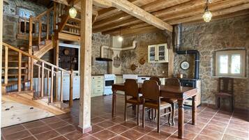 Een rustiek interieur met een houten trap, een eethoek met tafel en stoelen, een keuken met witte kasten en stenen muren.