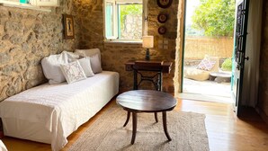 Quarto com paredes de pedra, uma cama, uma mesa e vista através de uma porta aberta.