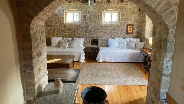 Um quarto com paredes de pedra, duas camas, uma mesa, um tapete e um balde.