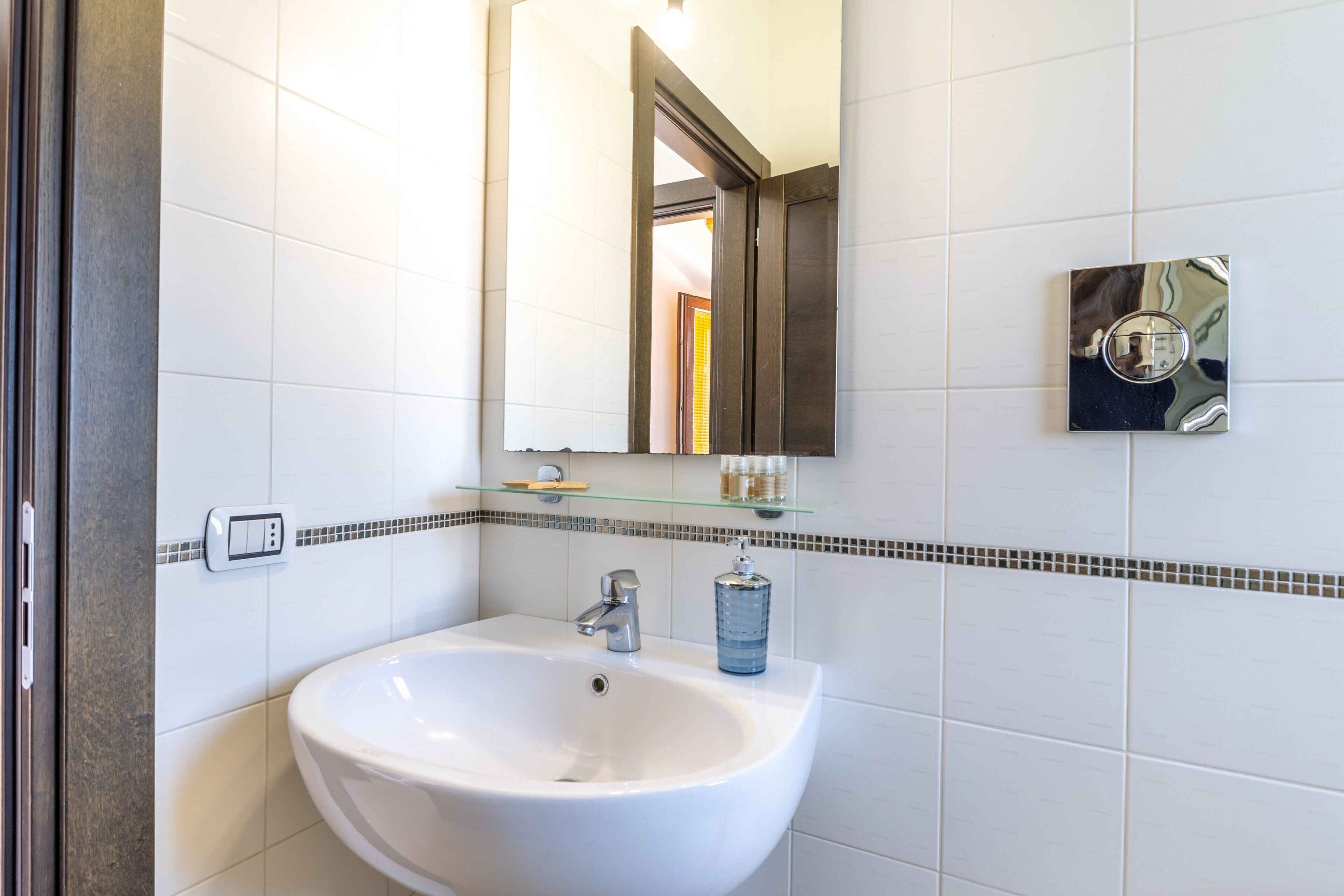 A bathroom with a white sink, a mirror, and a glass shelf with toiletries.