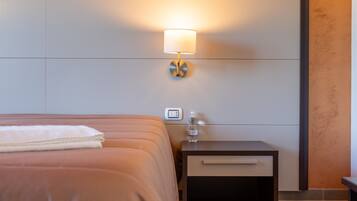 A hotel room with a bed, a nightstand with a lamp, a water bottle, and a thermostat.