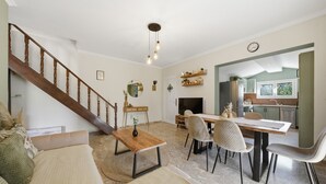A spacious living area with a wooden staircase, a dining table with chairs, a fireplace, and a kitchen visible through an open doorway. - Apartment 'Villa Logas 2' with Mountain View, Wi-Fi and Air Conditioning (Peroulades)