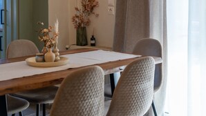 A dining area with a wooden table, beige chairs, a vase with dried flowers, and a bottle on the side table. - Apartment 'Villa Logas 2' with Mountain View, Wi-Fi and Air Conditioning (Peroulades)