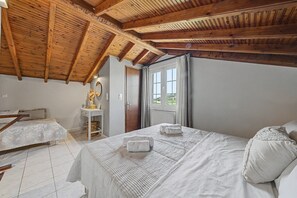 Ein Schlafzimmer mit Holzbalkendecke, einem Bett mit weißer Bettwäsche, einem Nachttisch und einem Fenster mit Vorhängen.