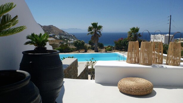 A poolside view with a clear view of the sea, a white building, and some potted plants. - Villa 11.7 – Luxus über dem Elia Beach, Mykonos (Elia)