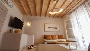 A room with a wooden ceiling, a flat-screen TV, a sofa with cushions, a small table, and a window with curtains. - Villa 11.7 – Luxus über dem Elia Beach, Mykonos (Elia)