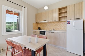 A modern kitchen with wooden cabinets, a white refrigerator, a microwave, and a dining table with chairs. - Studio Apartment '4' with Mountain View, Wi-Fi and Air Conditioning (Syvota)