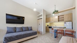 Un apartamento moderno con sofá cama, comedor con sillas, cocina con armarios de madera y televisor de pantalla plana montado en la pared.