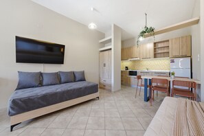Eine moderne Wohnung mit Schlafsofa, Essbereich mit Stühlen, Küche mit Holdekor und einem wandmontierten Flachbildfernseher.