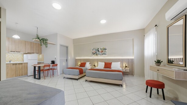 Ett modernt hotellrum med ett litet kök, två sängar, en matplats och en stor spegel.