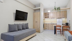 Ett modernt vardagsrum med en soffa, en platt-TV, träskåp, en köksdel med ett kylskåp och ett matbord med stolar.