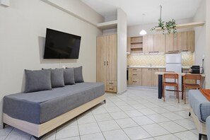 A modern living room with a sofa, a flat-screen TV, wooden cabinets, a kitchen area with a refrigerator, and a dining table with chairs. - Studio Apartment '5' with Shared Garden, Wi-Fi and Air Conditioning (Syvota)