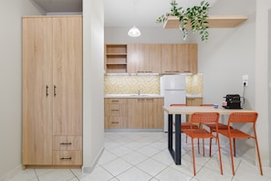 A kitchen with wooden cabinets, a white refrigerator, a tiled backsplash, and a dining table with orange chairs. - Studio Apartment '5' with Shared Garden, Wi-Fi and Air Conditioning (Syvota)