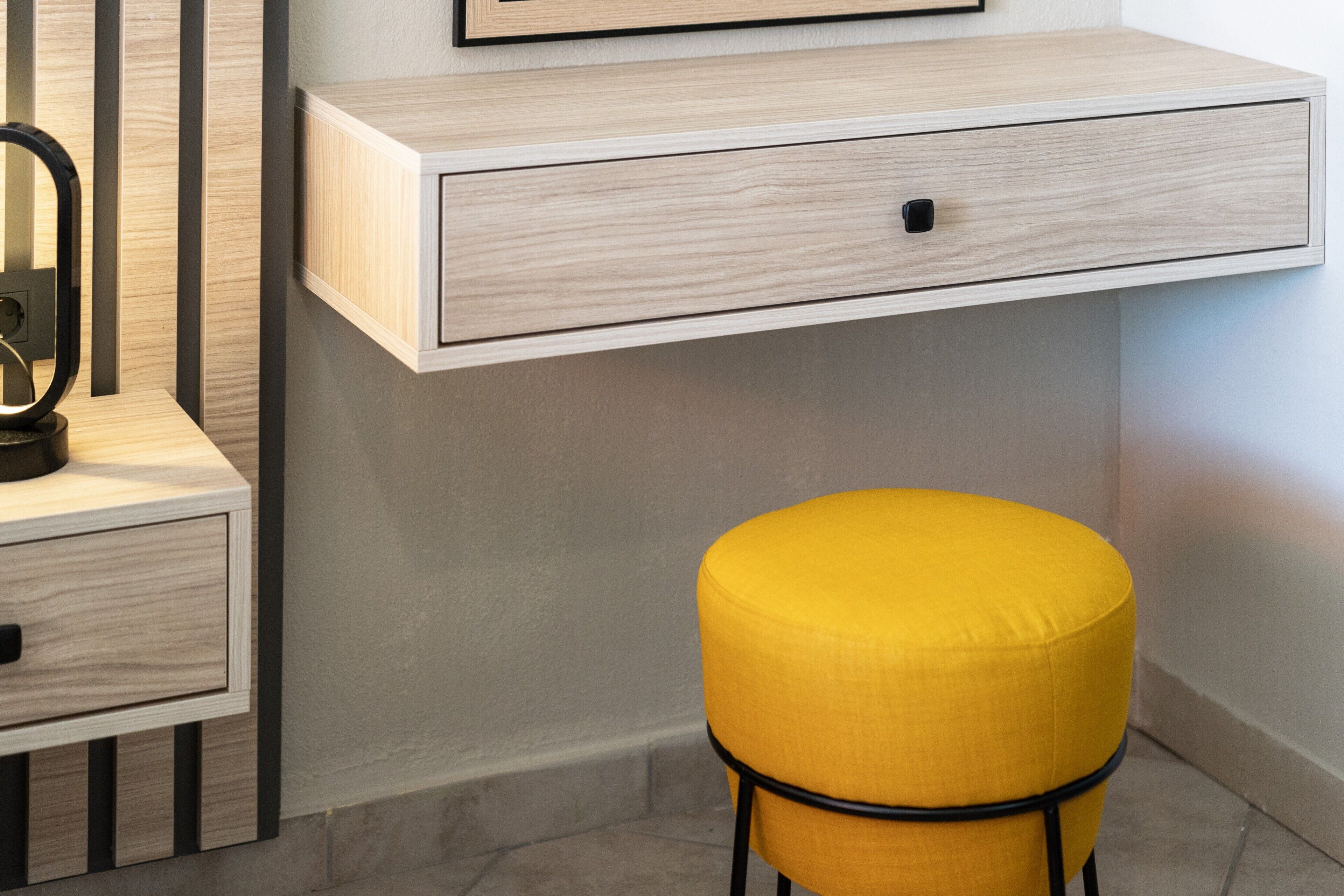 Een moderne kamer met een houten bureau, een geel gestoffeerde kruk en een spiegel aan de muur.