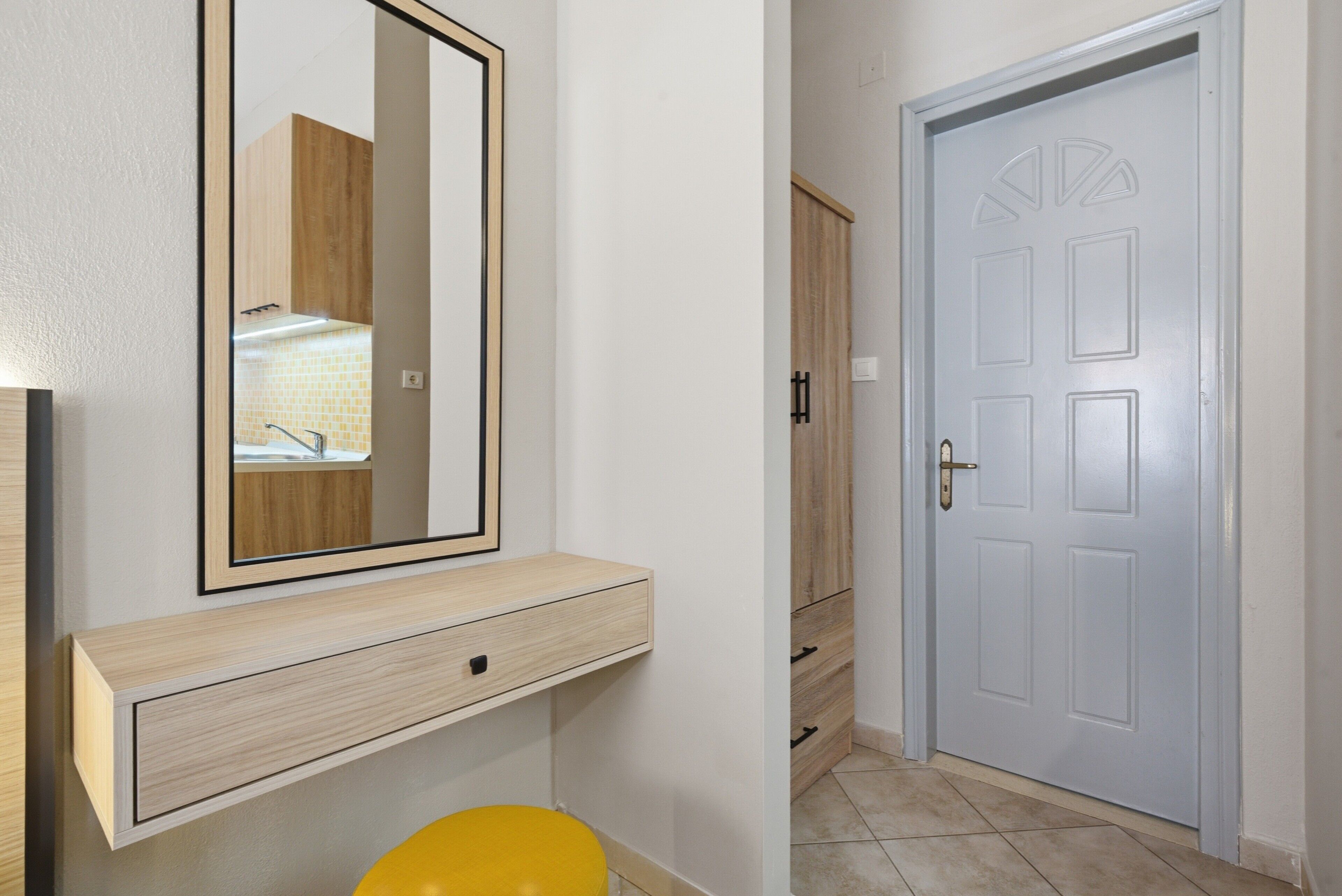 Une salle de bain avec un miroir, une chaise jaune, un meuble en bois et une porte blanche.