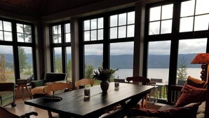 Un espace repas comprenant une table, des chaises et une vue sur un lac et des montagnes, grâce à de grandes fenêtres.