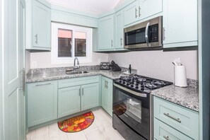Una cocina con armarios color esmeralda, un microondas de acero inoxidable, una estufa a gas y una encimera de granito.