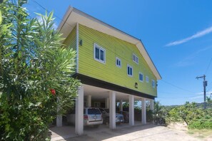 Una casa de dos pisos con fachada verde y un porche cubierto, con un automóvil estacionado al frente.