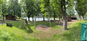 A park with swings, a picnic table, a small cabin, and a lake in the background.