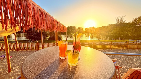 Ein runder Tisch mit Getränken und Blick auf einen See bei Sonnenuntergang.