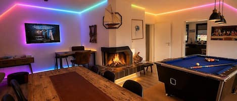 A cozy room with a pool table, a fireplace, and ambient lighting.