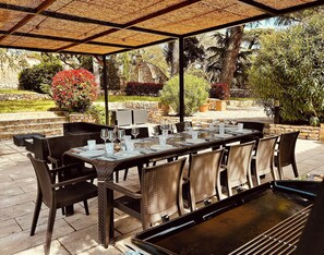 Un espace extérieur aménagé pour les repas, avec un patio couvert, des meubles en osier et un mur en pierre en arrière-plan.