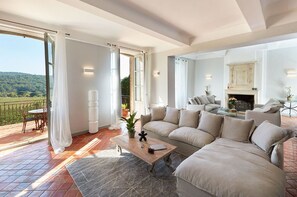Ein großzügiges Wohnzimmer mit einer großen Couch, einem Couchtisch und einem Kamin. Ein Balkon mit Tisch und Stühlen bietet Blick auf die Landschaft.