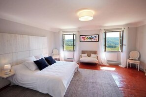 Une chambre à coucher comprenant un lit, des tables de chevet, une chaise, un canapé et une fenêtre donnant sur un beau paysage.