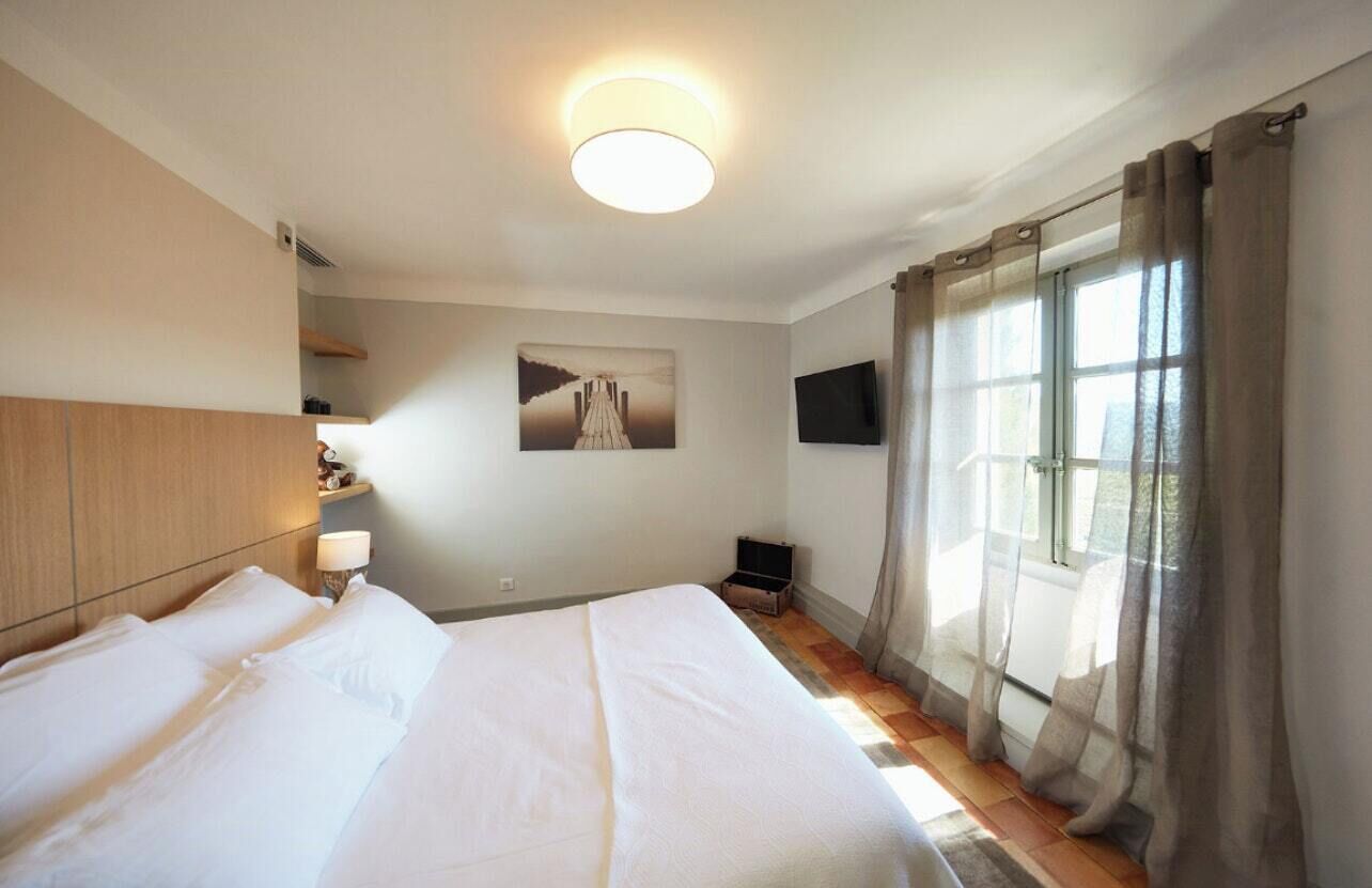 Une chambre d’hôtel avec un grand lit, un téléviseur à écran plat, un tableau au mur et une fenêtre avec des rideaux.