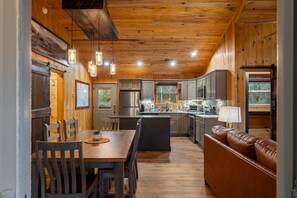 Ein Interieur einer Holzhütte mit Esstisch, Stühlen, einer Couch, einer Küche mit Geräten und hängenden Pendelleuchten.