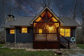 Eine Hütte mit Steinverkleidung, einer Holzdielen-Terrasse und einem sternenübersäten Nachthimmel, der durch die Fenster sichtbar ist.