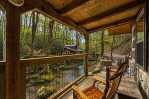 Eine Holzhütte mit Veranda mit Blick auf eine bewaldete Landschaft und einen kleinen Bach.
