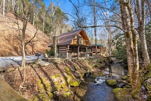 Eine Holzhütte mit Steinunterbau und einer Terrasse mit Blick auf einen Bach.
