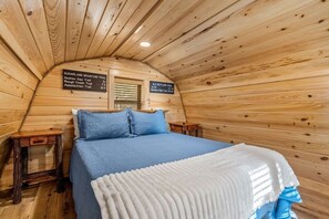 Ein gemütliches Blockhauszimmer mit Holzbalkendecke, einem Bett mit blauer Bettwäsche und einem Schild, das Wanderwege in der Umgebung auflistet.