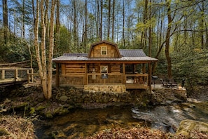 Eine rustikale Holzhütte mit Stein Fundament, Holzwänden und einem Metall Dach, umgeben von einem Wald und einem Bach.