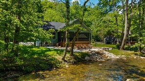 A cabin with a stone patio, surrounded by lush greenery and a clear stream. - Waterfront Cabin Swim, Fish or Float the Creek! (Cosby)
