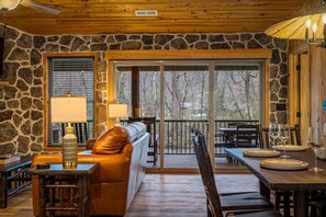 Un interior acogedor con paredes de piedra, un sofá de cuero, una mesa de comedor preparada para cuatro personas y un balcón con vistas.
