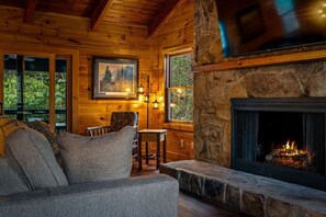 A log cabin interior with a stone fireplace, wooden walls, a sofa, and a dining table. - Walking distance to best Smoky Mountain Hiking (Cosby)