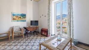 Una stanza con una grande finestra, un quadro appeso al muro, un tavolo in legno, una panca e un televisore.