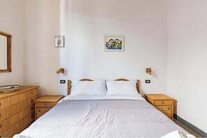 Een slaapkamer met een bed, houten nachtkastjes, een dressoir en twee wandlampen.