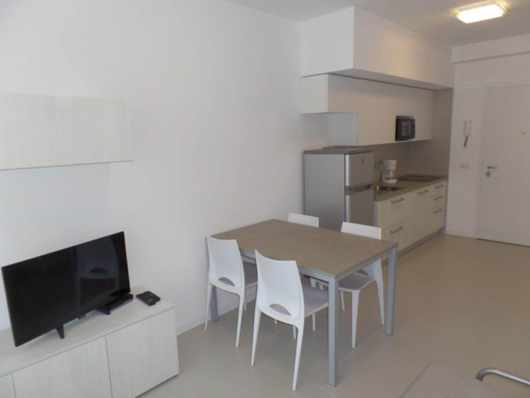 Une cuisine de taille réduite comprenant une table à manger, des chaises, un téléviseur et un réfrigérateur.
